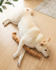 Light-colored dog lying with a brown sausage plush toy
