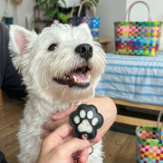 Black paw-shaped fur keepsake keychain held beside a white dog